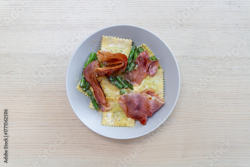 A plate of cheese ravioli with prosciutto on top.