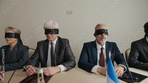 PAN waist up of group of international delegates sitting at table during political meeting, wearing blindfolds, appearing uncertain or puzzled, symbolizing disagreement or lack of understanding