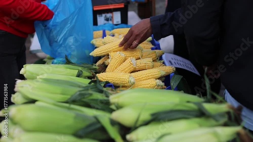 Woman buying fresh corn at a market, with the vendor handing over the goods in a bag and receiving cash payment.