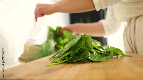 A woman carefully arranges fresh spinach leaves on a kitchen table, preparing healthy ingredients for cooking a homemade meal.