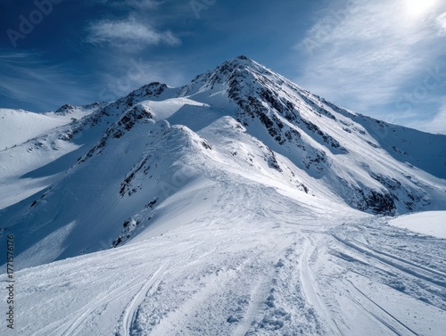 Panoramic View of Majestic Snow-Capped Mountain Peak Winding Ski Tracks on Slopes Bright Blue Sky with Wispy Clouds Winter Wilderness Adventure