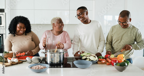 Happy black family cooking inside kitchen at home - Daughter, son, father and mother having fun preparing vegetarian lunch - Holidays and healthy food concept -  Main focus on boy face