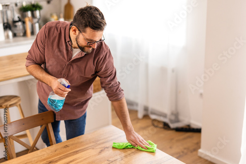Fotografie A man is cleaning a table at home, wiping down the surface to maintain a clean and organized space