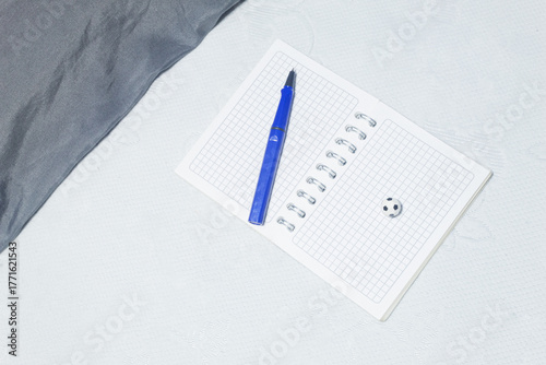 Small soccer ball next to a pen on a blank notebook on a white bedspread