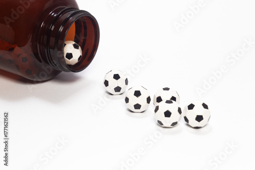 Tiny soccer balls coming out of a medicine bottle on a clean white surface. Sport for a healthy life. Ball-shaped pills