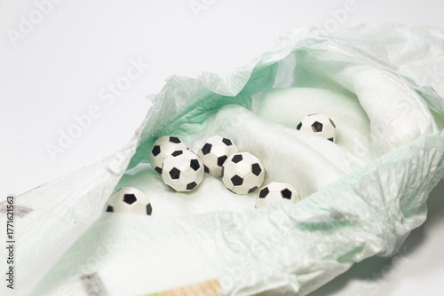 Small soccer balls inside a white disposable diaper on a white background