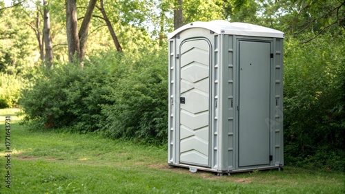 Portable restroom in a grassy area surrounded by bushes.