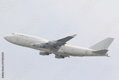 An unmarked, all-white large cargo jet airplane climbing after takeoff against a plain overcast sky.