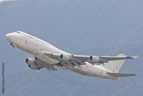 An unmarked, all-white large cargo jet airplane climbing after takeoff against a plain overcast sky.