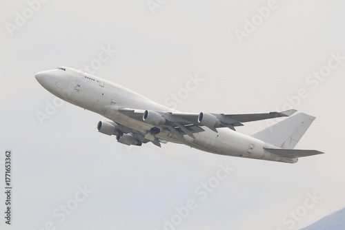 An unmarked, all-white large cargo jet airplane climbing after takeoff against a plain overcast sky.