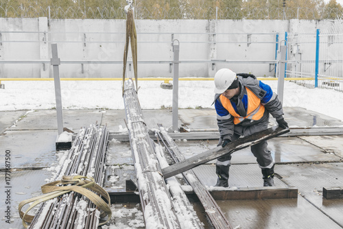 A construction worker in winter gear lifts steel beams at a construction site. The scene captures the industrious atmosphere of winter construction work.