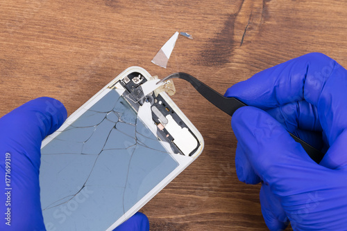 The wizard uses tweezers to remove glass fragments from the smartphone screen, close-up