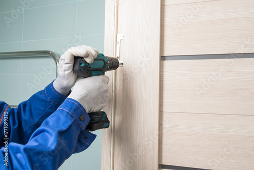 The master installs the door hinge using an electric screwdriver, close-up