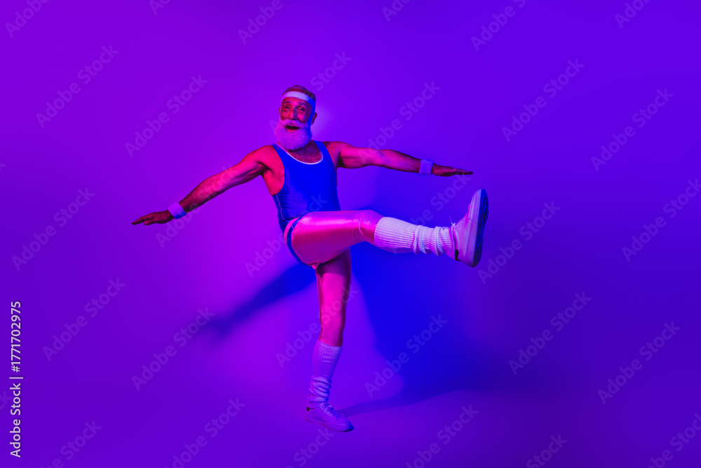 Naklejka premium Energetic bearded senior athlete in a retro jumpsuit performing a dynamic kick under purple blue neon lights