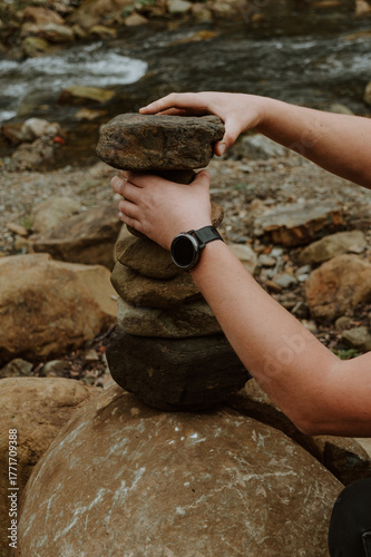 Close up of male hands stacking stones into a balancing tower on the bank of a mountain river. Symbol of harmony, balance, mindfulness, and relaxation in nature.