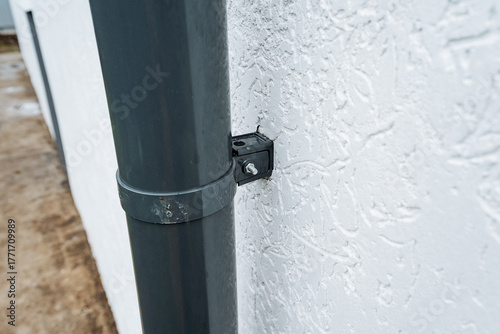 inspecting stained gray downspout exterior, closeup of stained gray downspout on textured wall, visual inspection of dark gray downspout with stains on textured wall outside