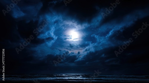 Full moon amidst dramatic dark clouds, over moonlit ocean waves at night, coastal seascape with atmospheric sky, wide angle view, copy space.