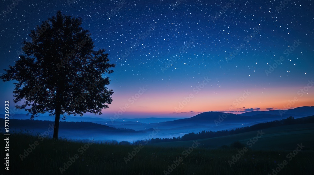 Fototapeta premium A lone tree stands against a starry sky, with a mountain range in the background. The tree is silhouetted against the colorful hues of the sunset, casting a warm glow on the landscape. 