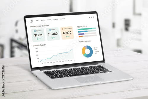 Open laptop on light wooden desk showing startup performance dashboard with growth charts, client metrics, and top products in modern workspace