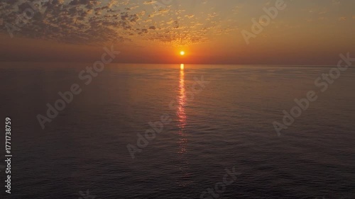 A tranquil drone shot of a stunning sunrise over calm sea waters, with a peaceful horizon and subtle clouds reflecting warm golden tones. Antalya, Turkey