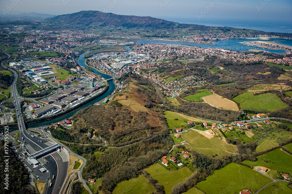 Obraz premium The aerial view captures the beautiful landscapes around Peage Biriatou and Hendaye, featuring lush greenery, winding rivers, and a coastal town under a clear blue sky.
