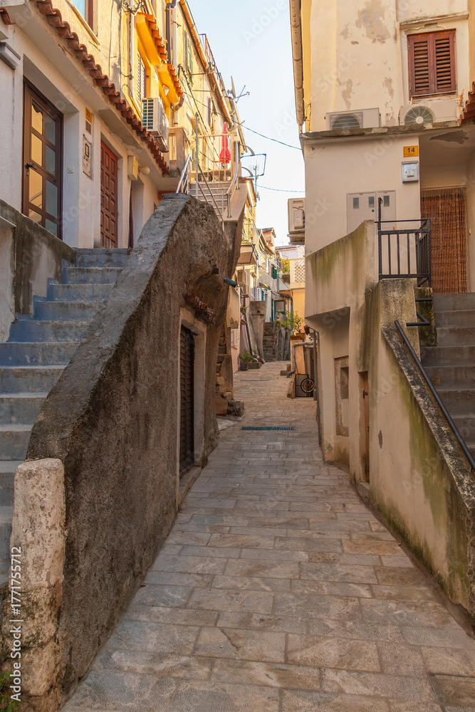 Fototapeta premium Narrow stone pathway in picturesque mediterranean village street scene. Baska, Krk island, Croatia