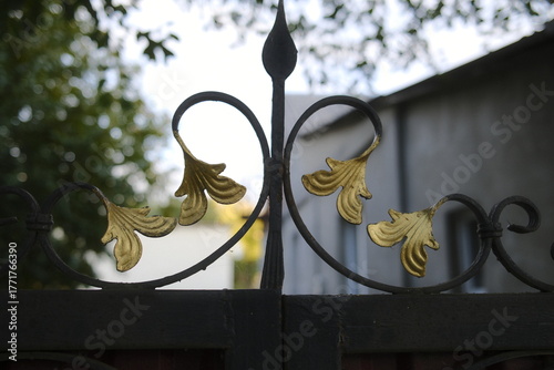 Decorative iron gate with gilded leaves in a garden setting.