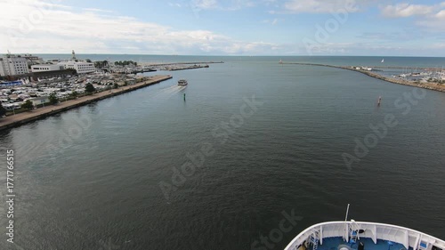 Aerial view from a ship entering a calm seaport on a sunny day. Coastal city, marina, and horizon with clear blue sky. Maritime travel and summer vacation concept