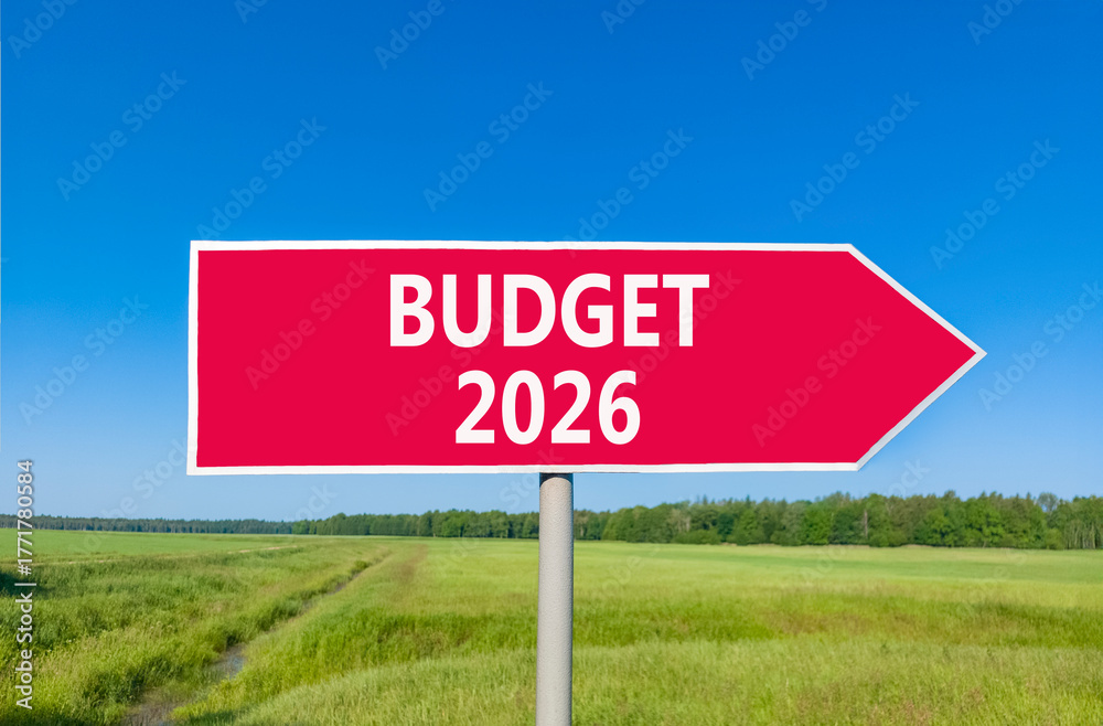 Obraz premium Budget 2026 symbol. Concept words Budget 2026 on beautiful red road sign. Beautiful green grass field forest and blue sky background. Business and budget 2026 concept. Copy space.
