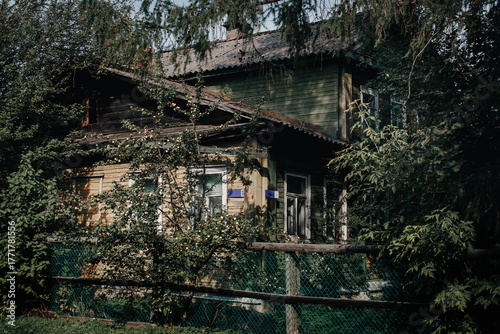 Abandoned rustic wooden house overgrown with trees and vines, behind a chain-link fence — perfect for themes of decay, nostalgia, mystery, and nature reclaiming man-made structures.