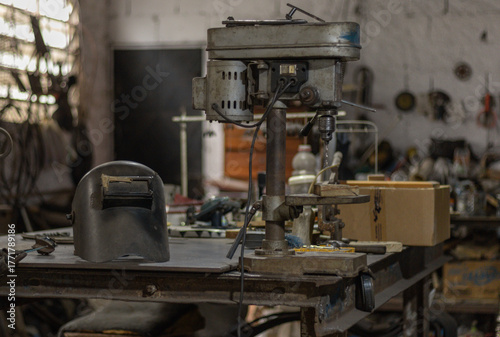 Workshop tools on a bench, a vintage drill press and welding helmet illustrating concepts of craftsmanship, repair, and industry