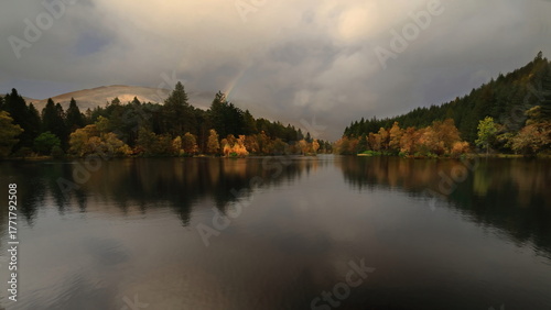Glencoe Lochan surrounded by tall Canadian redwoods and Douglas firs planted in the 1890s, under a cloudy rainy sky with rainbow. Glencoe-Scotland-041