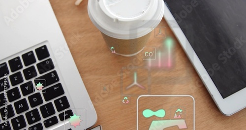 Presenting brown coffee cup displaying floating eco icons on office desk, with laptop and tablet