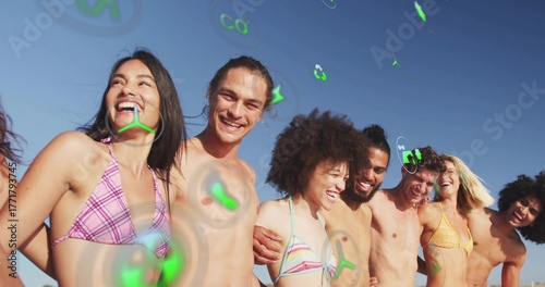 Quadro su tela Laughing friends wearing colorful swimwear standing on beach, with floating gree