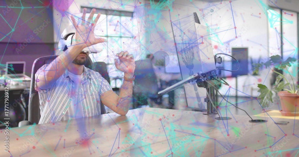 Obraz premium Gesturing using VR headset, man wearing striped shirt at open office desk with monitor, copy space