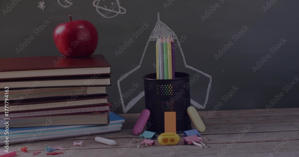 Obraz premium Holding colored pencils, pencil holder sitting in class with apple-topped textbooks and chalkboard