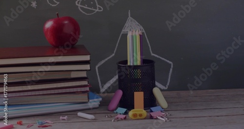 Holding colored pencils, pencil holder sitting in class with apple-topped textbooks and chalkboard