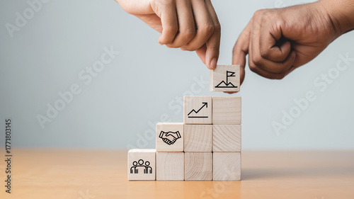Minimalist business concept with wooden blocks forming stairs, two hands placing final cube, symbolizing teamwork, growth, unity, leadership, success, and partnership on bright table.