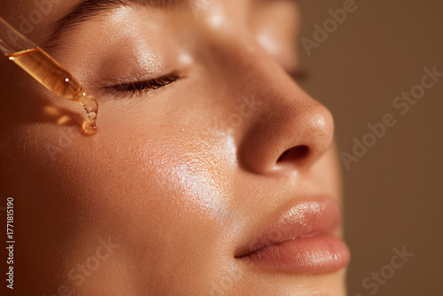 Golden skincare cosmetic serum pouring and flowing from pipette on beautiful female woman beauty models face detail. Gentle natural moisturizing hydration and skin care routine.