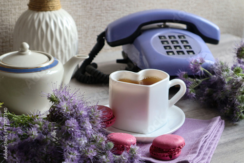 Autumn tea party: a white cup of tea in the shape of a heart with purple flowers against a backdrop of an old telephone