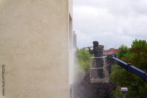 Unrecognizable man cleaning facade surface from lifting platform with high pressure stream of water