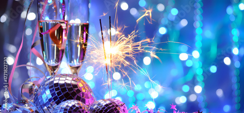 Festive new year's eve celebration with champagne flutes sparklers and disco balls against a sparkling blue bokeh background creating a party atmosphere