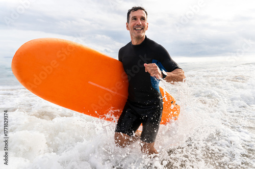 Sticker Middle aged sportive handsome man learning surfing and running in the waves hold