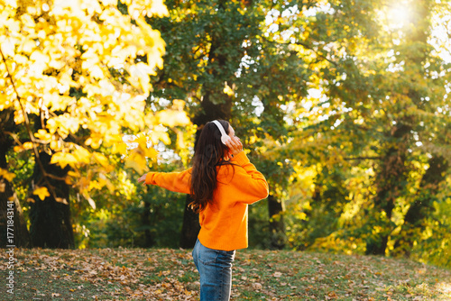 Happy woman walking among autumn trees listening to music with headphones