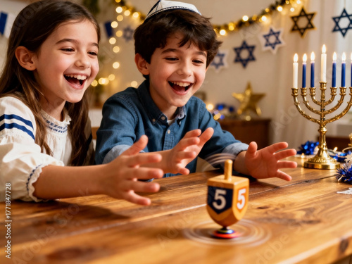 Two children celebrate Hanukkah, a young Caucasian girl with long brown hair and a young Caucasian boy with curly brown hair play with a dreidel on a wooden table.