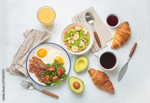 Breakfast table healthy foods fried eggs, bacon, oats fruit, avocado, croissants, coffee, orange juice on white background top view