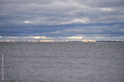 Sea horizon with distant industrial skyline beneath layered cloudy sky.
