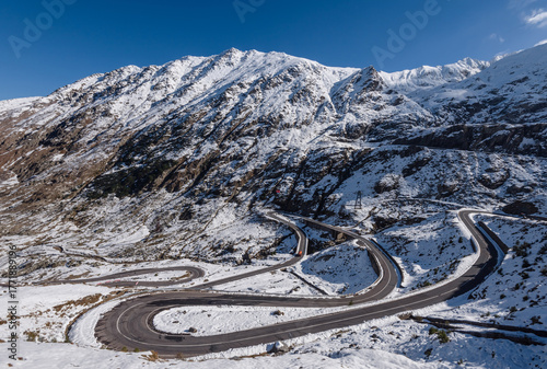 panoramic view of the Transfagarasan Highway winding through the snowy peaks of the Carpathian Mountains in Romania. Scenic mountain road under bright sunlight, famous travel destination in Europe.