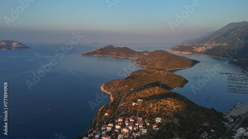 Aerial drone view of Kas Peninsula at sunrise, with calm blue sea, anchored boats, and mountains glowing in the first morning light. Turkey