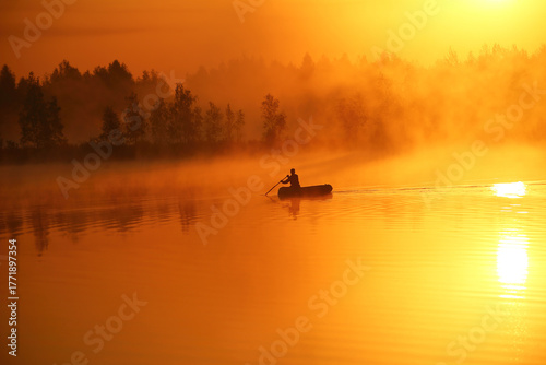 On a foggy morning at dawn, a boat with a fisherman sails in silence